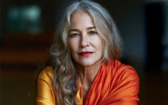 A portrait of a woman with long gray hair wearing a yellow and orange garment.