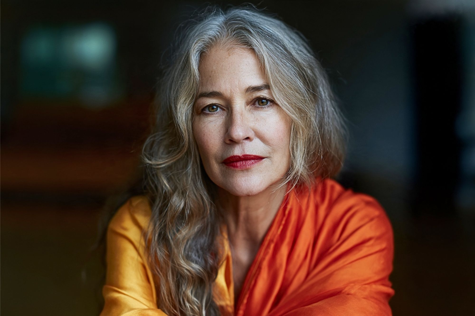A portrait of a woman with long gray hair wearing a yellow and orange garment.