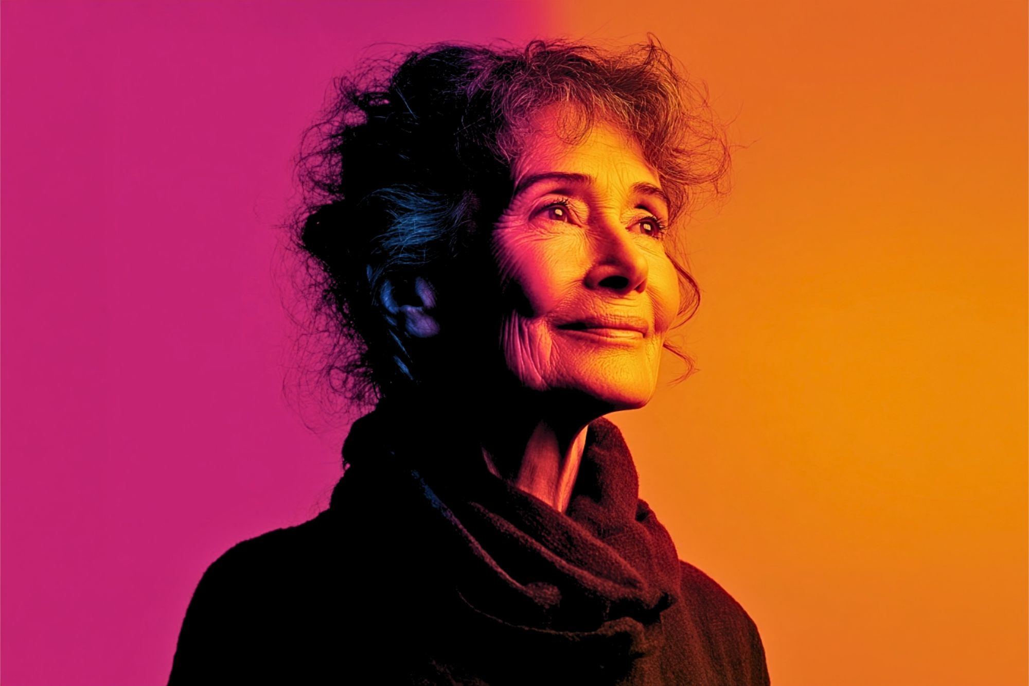 An older woman with curly hair looking upward against a vibrant magenta and orange gradient background.