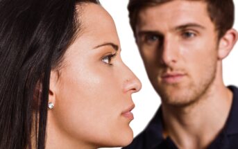 A woman is shown in sharp profile in the foreground, with a man standing slightly out of focus in the background. Both have neutral expressions and are set against a white backdrop.