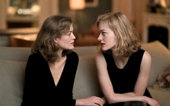 Two women with shoulder-length blonde hair sit on a sofa facing each other.