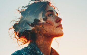A double exposure image of a young woman with freckles looking upward, her profile blending with a landscape of trees and sunlight, creating a dreamy, artistic effect against a pale sky background.