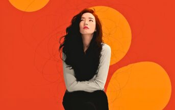 A woman with long, wavy dark hair sits with arms crossed, gazing upward. She wears a light sweater and dark scarf. The background is bright orange with large, overlapping yellow circles.