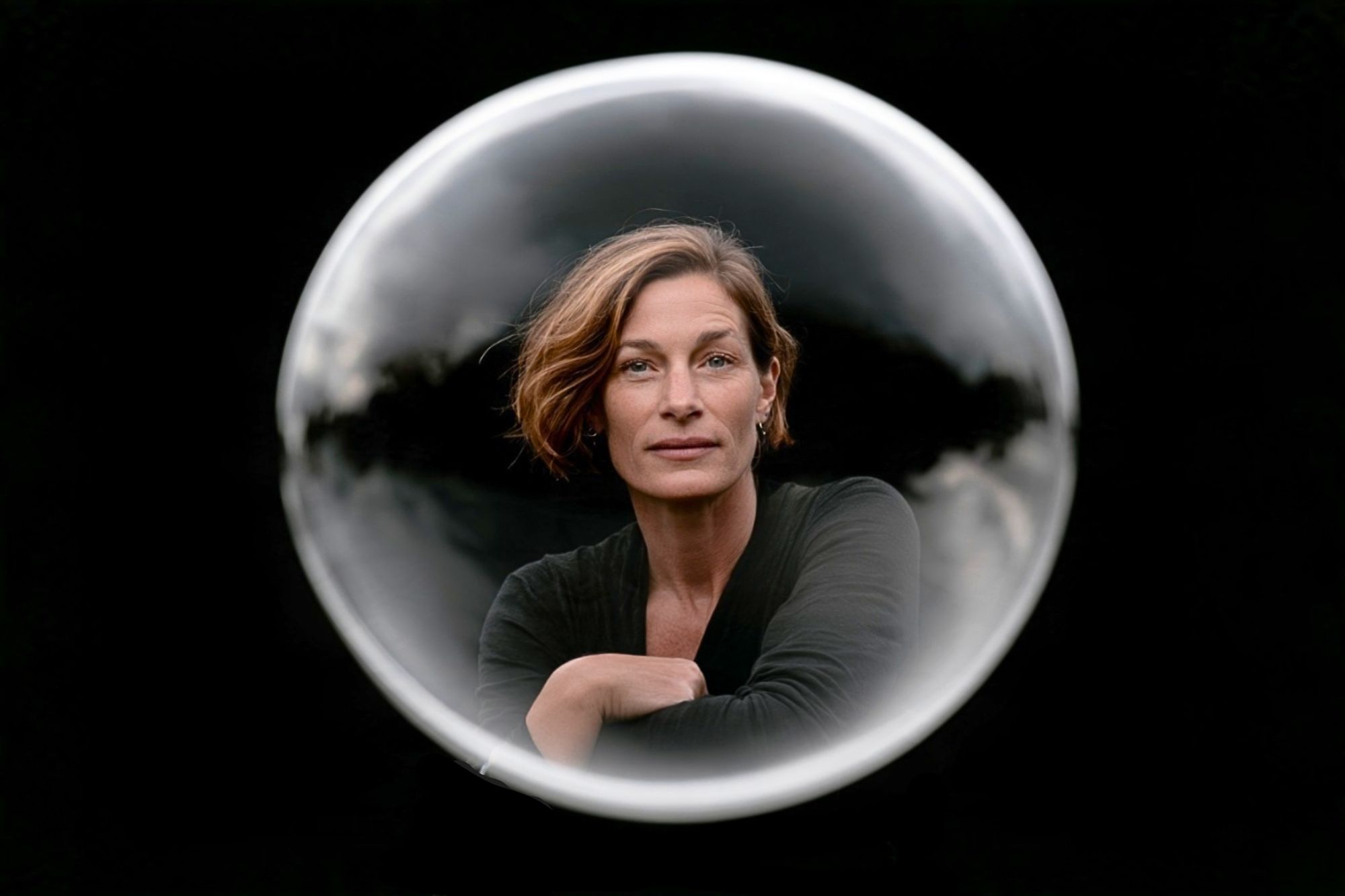 A woman looking forward, framed within a circular glass sphere against a black background.
