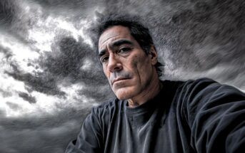 A man with dark hair and a serious expression poses in front of a cloudy, dramatic sky. The image has an artistic, painted effect with textured lines and swirling patterns. He wears a dark shirt.