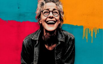 A smiling older person with glasses and short gray hair wears a denim jacket in front of a colorful painted background with red, teal, and yellow sections.