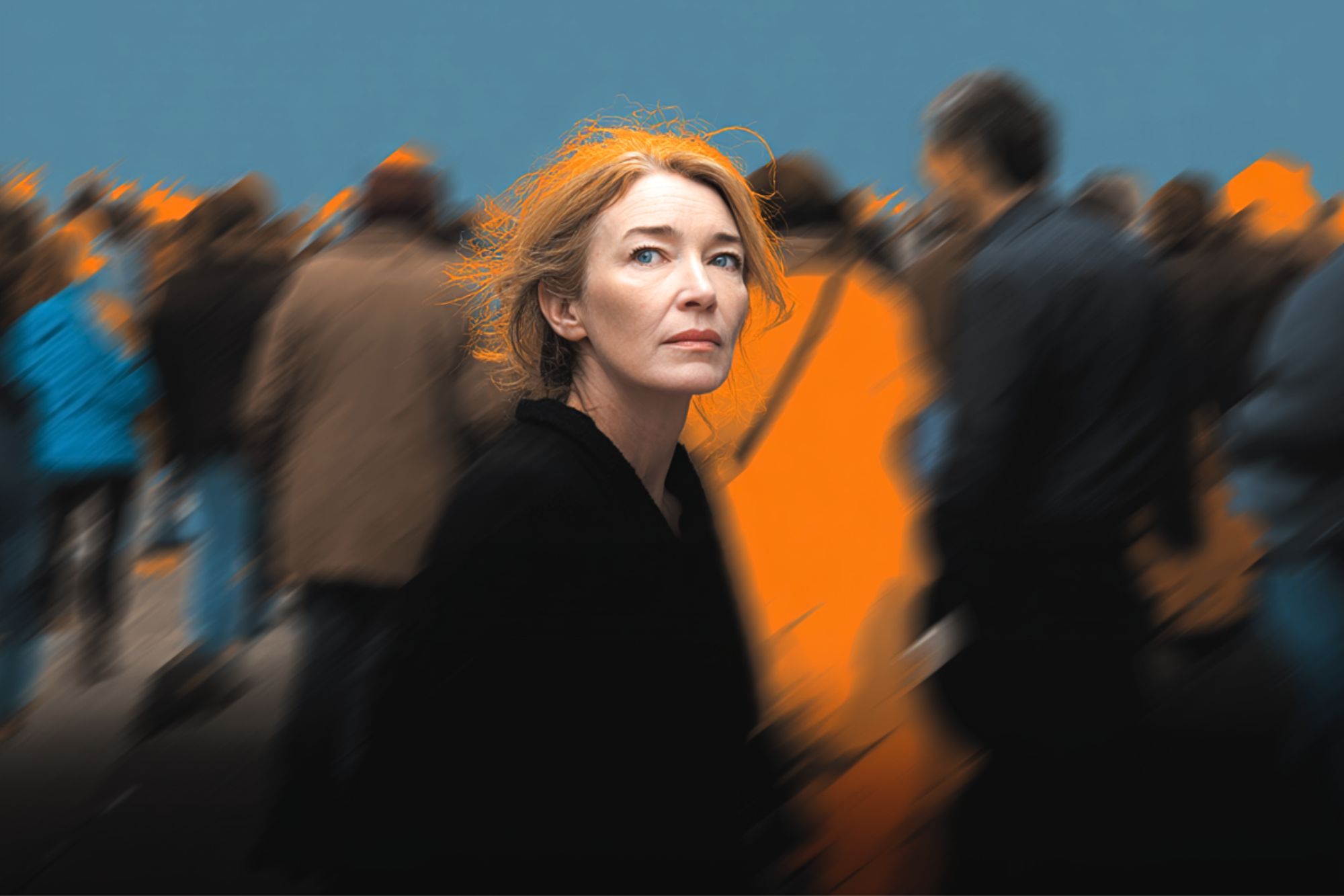 A woman with reddish hair looks up pensively, standing still amid a blurred crowd of people moving around her. The background is dark and blue, with orange highlights, making her stand out in sharp focus.
