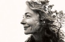 A black and white double exposure image of a smiling woman’s side profile blended with silhouettes of tall trees, creating an artistic and serene effect.