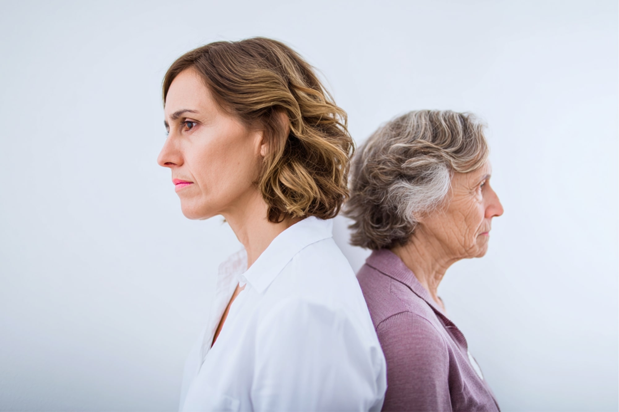 Two women, one younger and one older, stand back-to-back, both looking serious and facing away from each other against a plain white background.
