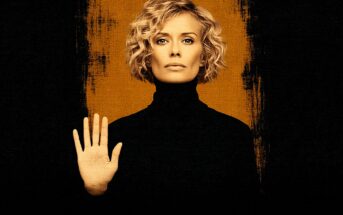 A woman with short, curly blonde hair and a serious expression faces forward, wearing a black turtleneck and holding up her left hand in a stop gesture. The background is black with a vertical orange stripe behind her.