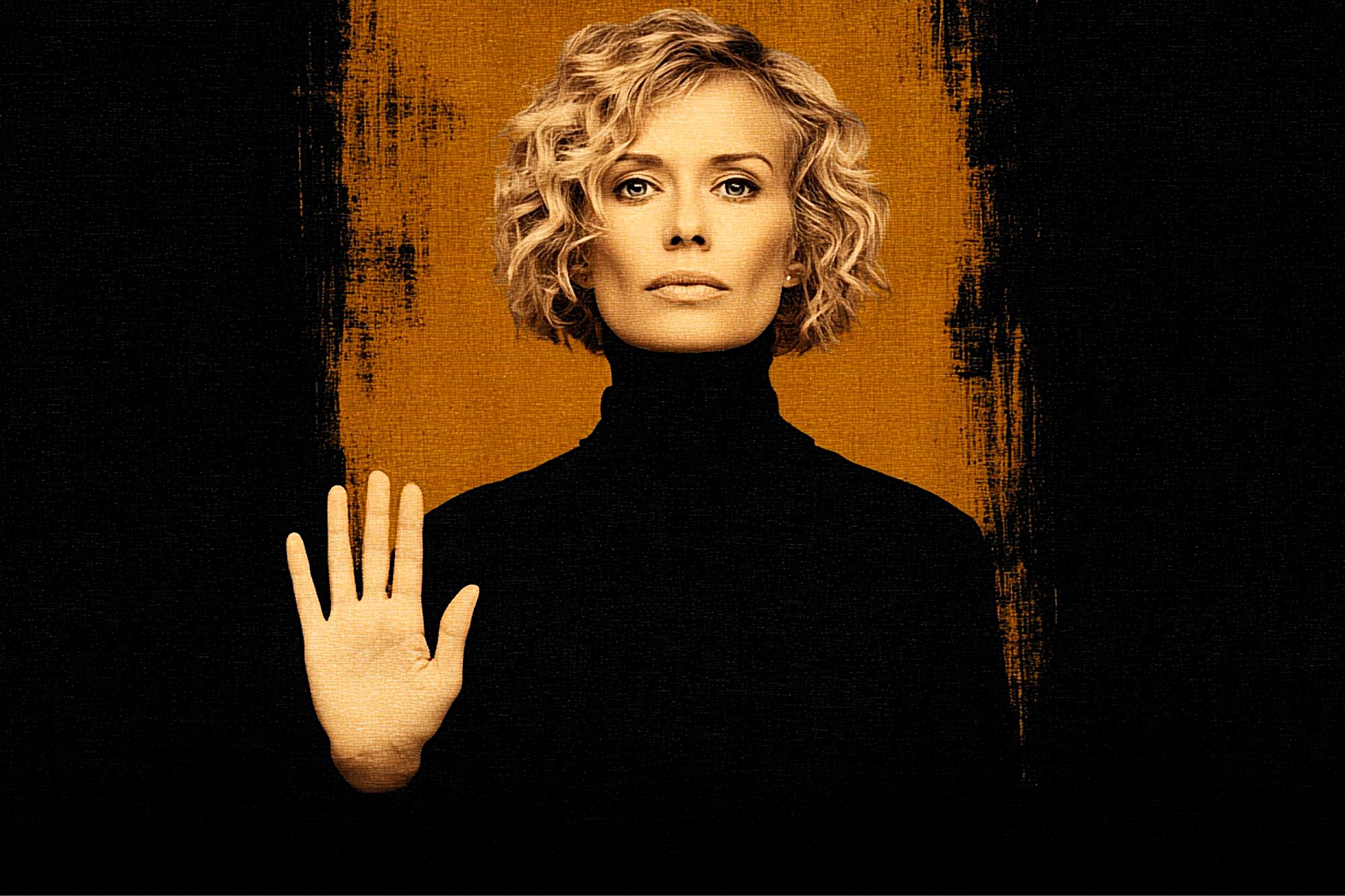 A woman with short, curly blonde hair and a serious expression faces forward, wearing a black turtleneck and holding up her left hand in a stop gesture. The background is black with a vertical orange stripe behind her.
