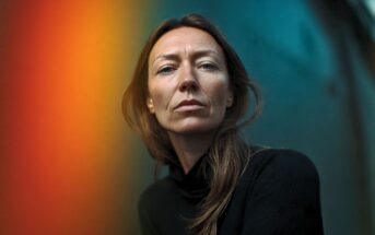 Portrait of a woman looking directly at the camera with a gradient of orange and teal light across the background.