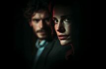 A woman with an intense expression is lit dramatically in the foreground, while a man with curly hair and a beard is blurred in the dark background, creating a mysterious and moody atmosphere.