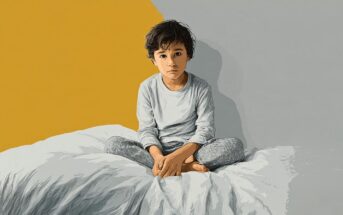 A young child with dark hair sits cross-legged on a bed against a split yellow and gray background.