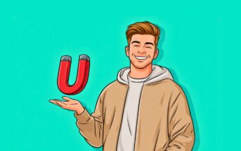 A smiling man in a tan jacket and hoodie holds a red horseshoe magnet in his open hand against a bright turquoise background.