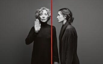 A grayscale image of two women separated by a vertical red line; the older woman on the left faces forward with her palm raised, while the younger woman on the right faces sideways. Both wear dark turtlenecks.