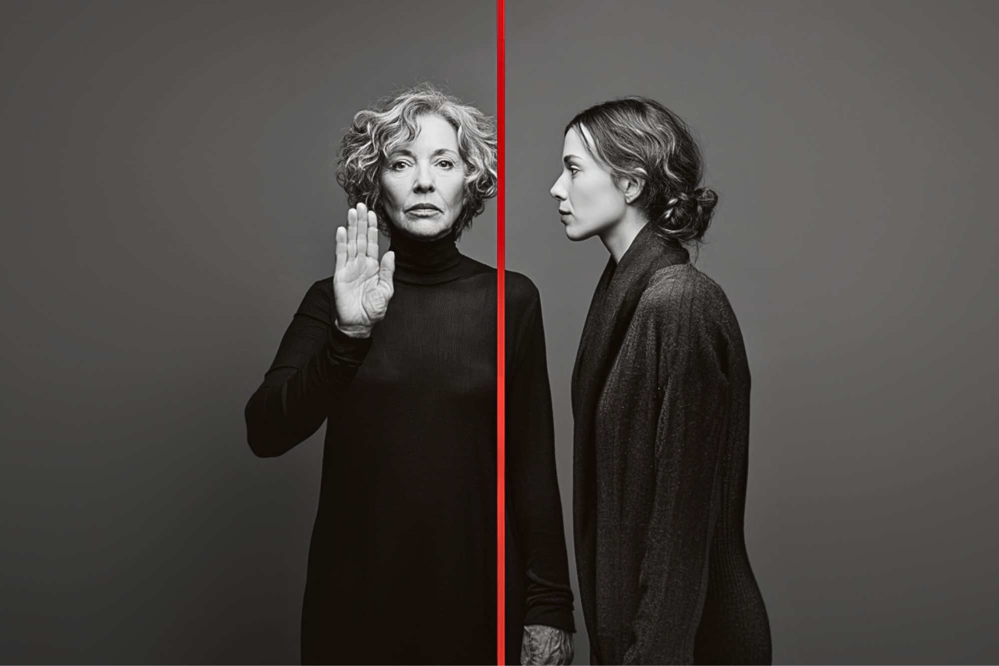 A grayscale image of two women separated by a vertical red line; the older woman on the left faces forward with her palm raised, while the younger woman on the right faces sideways. Both wear dark turtlenecks.