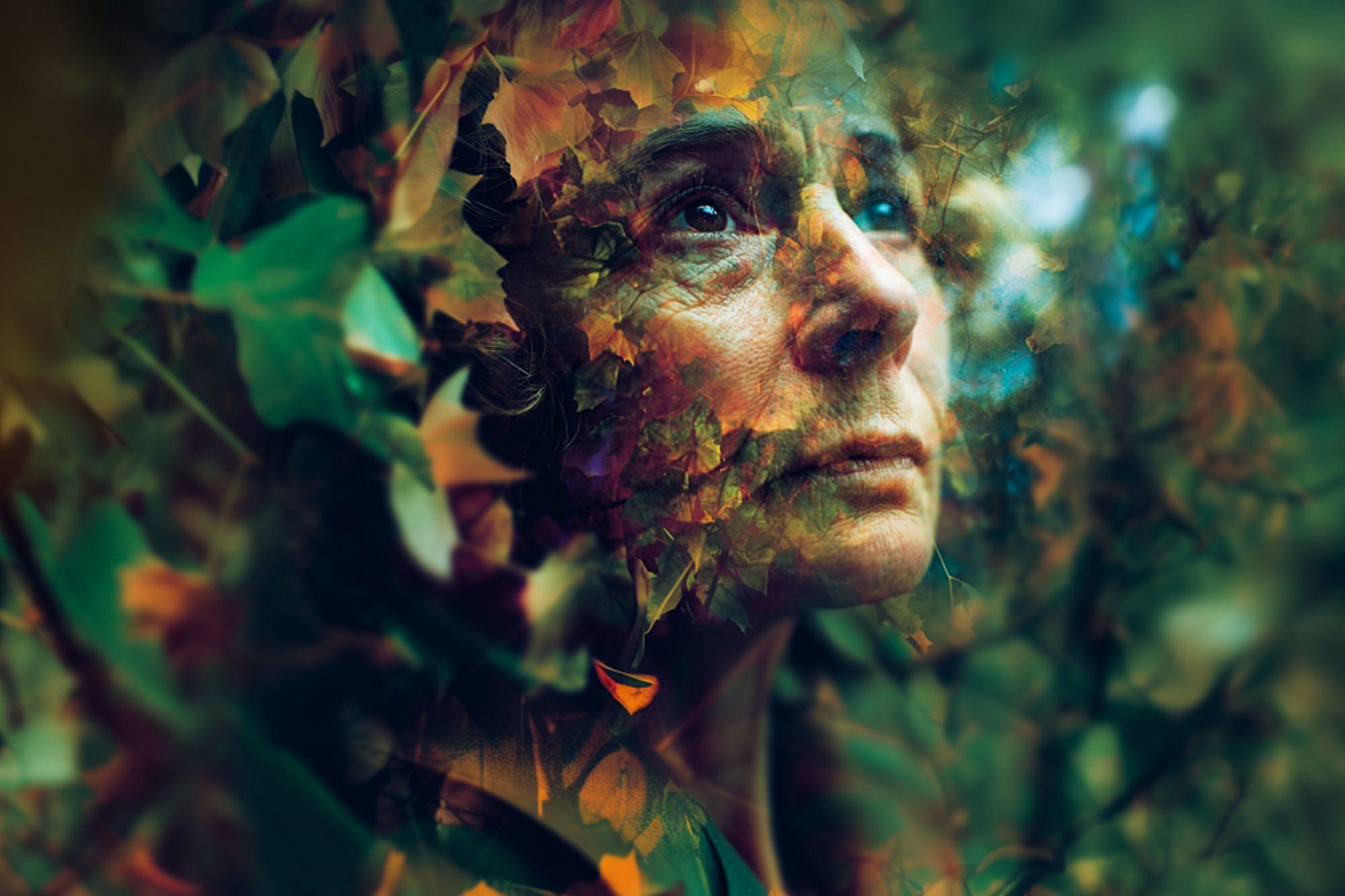 A woman’s thoughtful face is blended with autumn leaves and foliage, creating a dreamy, surreal effect as she gazes upward in a forest-like environment.