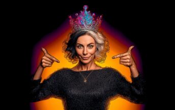 A woman with short gray hair wearing a colorful, ornate crown points at it with both hands. She smiles confidently, standing against a glowing orange and black background.