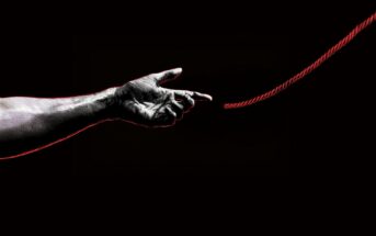 A grayscale hand stretches toward a red rope against a black background, with the fingers almost touching the rope, symbolizing connection or reaching out.