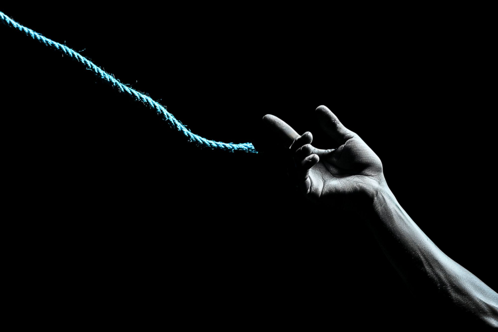 A dimly lit hand reaches out, fingers hooked around a blue rope against a black background, suggesting a moment of grasping or letting go.