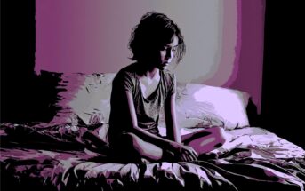 A person with short hair sits alone on a rumpled bed in a dim room with purple lighting, looking down with a thoughtful or somber expression.