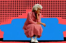 An older woman with white hair, wearing a red and white polka dot dress and white sneakers, sits thoughtfully with her chin on her hand in front of a blue couch on a red background with black dots.