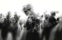 A grayscale image of a person with short hair and glasses, looking downward, is overlaid with multiple blurred silhouettes of people walking in different directions, creating a sense of introspection and crowd.