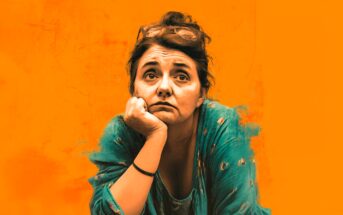 A woman with dark hair, wearing a teal top and glasses on her head, rests her chin on her hand and looks thoughtfully ahead, set against a bright orange background.