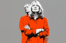 A man and woman stand together, both wearing bright orange shirts against a plain gray background. The woman stands in front with her arms crossed, while the man stands slightly behind, looking off to the side.