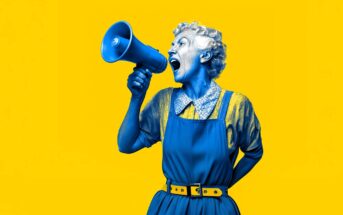 A person painted blue, wearing an apron and holding a megaphone, shouts with an expressive face against a bright yellow background.