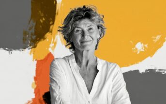 Portrait of a smiling mature woman against an abstract background of orange, white, and grey shapes.