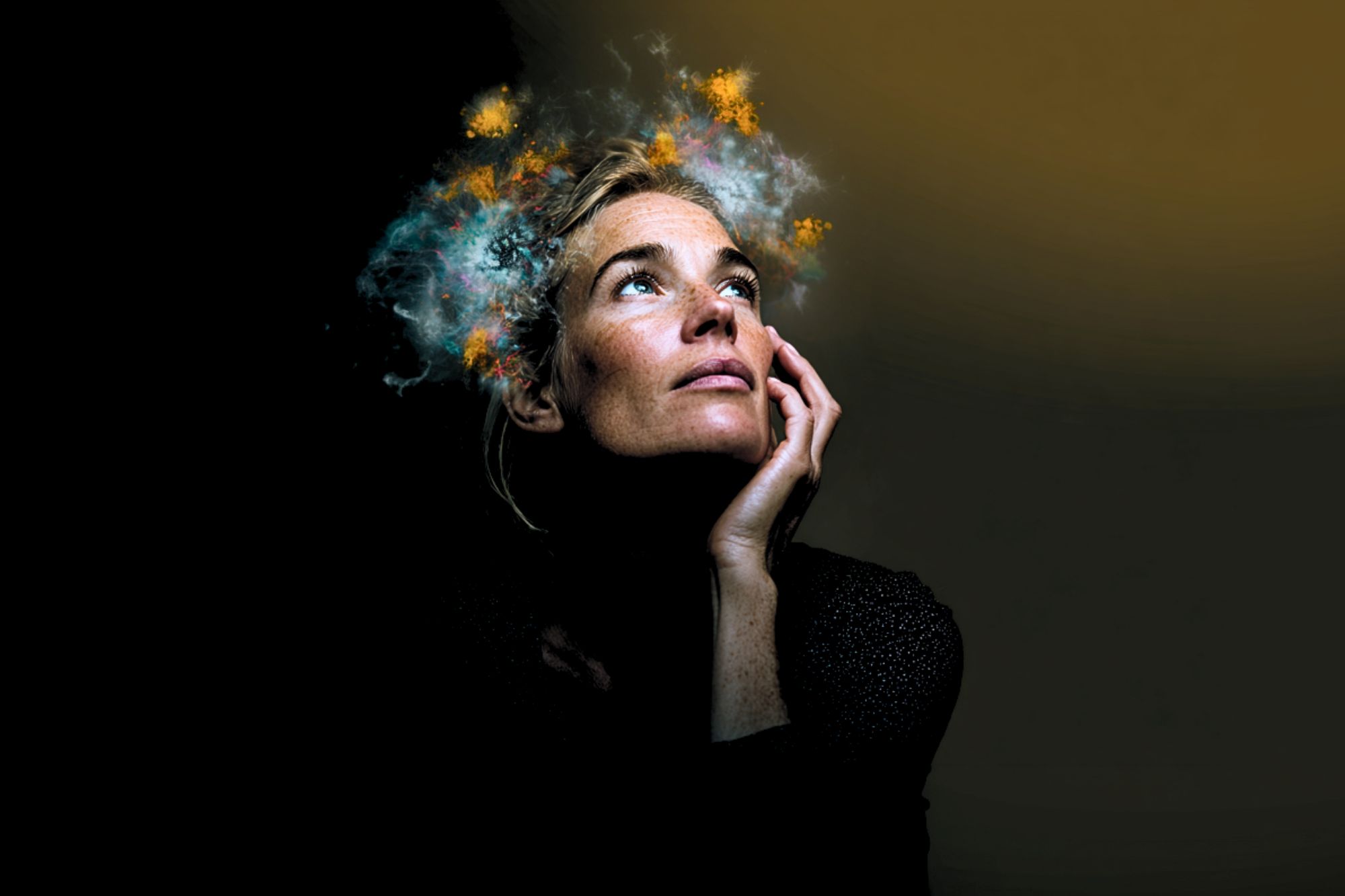 A woman gazes upward with her hand on her cheek, while bright, colorful clouds and sparks appear to emanate from her head against a dark background, symbolizing imagination or creativity.