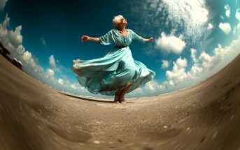 An older woman in a flowing blue dress joyfully dances barefoot on a sandy beach under a dramatic, cloudy sky, captured with a fisheye lens that curves the horizon.