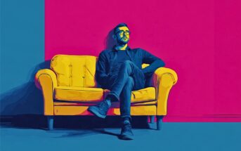 A man wearing glasses sits cross-legged on a yellow couch against a vibrant blue and pink background.