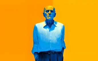An older man with a serious expression, illustrated in shades of blue, stands with his hands in his pockets against a vibrant yellow and orange background.