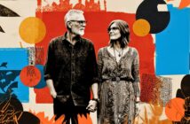 An older couple holding hands and smiling at each other stands against a colorful abstract background with bold patterns and shapes.