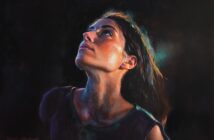 A realistic painting of a woman with long dark hair gazing upward, illuminated by dramatic, colorful lighting against a dark background. Her expression appears thoughtful or hopeful.