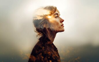 A double-exposure image of a woman in profile, looking thoughtful, with a bright sky and clouds blended into her hair and face, and a dark, wooded landscape merging into her silhouette.