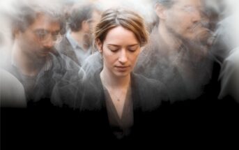 A woman stands with her head bowed, eyes closed, surrounded by blurred, indistinct figures in a crowd, creating an effect of isolation and introspection amidst others.