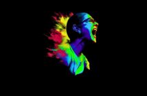 A stylized digital artwork of a person screaming, with vibrant neon colors—blue, green, yellow, and red—exploding behind them against a black background. The person wears glasses and their expression is intense.