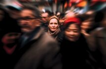 A woman stands still and looks ahead in a crowded, busy street. The people around her appear blurred, emphasizing her calm and focused presence amid the moving crowd.