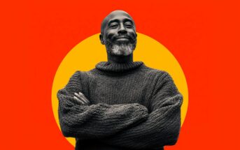 A man with a beard and mustache wearing a thick knit sweater stands with arms crossed, smiling confidently. The background features a large yellow circle on a vibrant red backdrop.