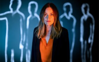 A woman standing in front of a wall featuring glowing outlines of figures.