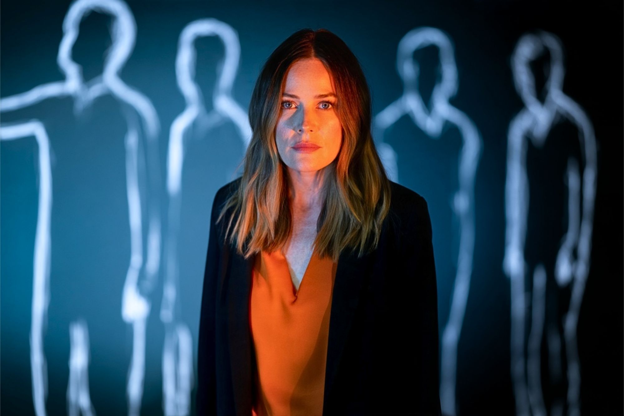 A woman standing in front of a wall featuring glowing outlines of figures.