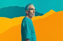 A man with short gray hair and a beard stands in profile, wearing a teal shirt against a vibrant, stylized background of yellow and blue mountains.