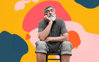 An older man with a white beard sits on a stool, resting his chin on his hand, looking thoughtful. He is in front of a vibrant yellow background with abstract pink, orange, and blue shapes.