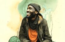 A smiling man in a green jacket, orange shirt, and beanie sits against a light-colored, artistic watercolor background, looking up and to the side.