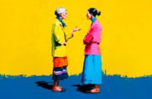 Two women wearing colorful clothes stand facing each other and conversing against a vibrant yellow background. One woman gestures with her hand while the other listens with arms crossed.