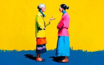 Two women wearing colorful clothes stand facing each other and conversing against a vibrant yellow background. One woman gestures with her hand while the other listens with arms crossed.